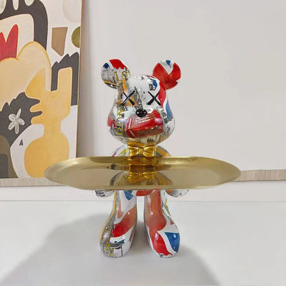Red, white, and blue patterned bear sculpture with X-shaped eyes on a gold display tray
